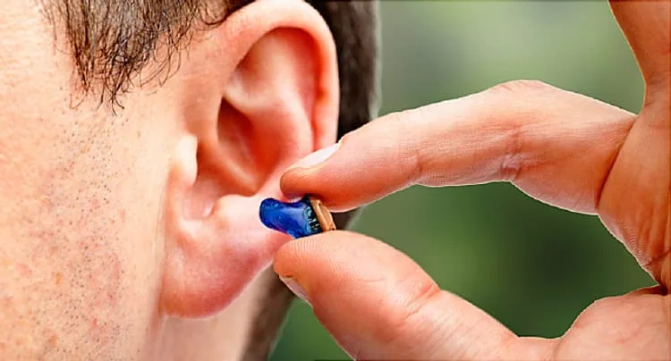 Person inserting small blue hearing aid into ear canal