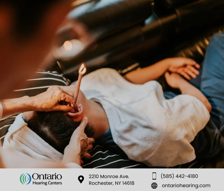 A person lying down with a towel wrapped around their head while another person holds a lit ear candle in the person