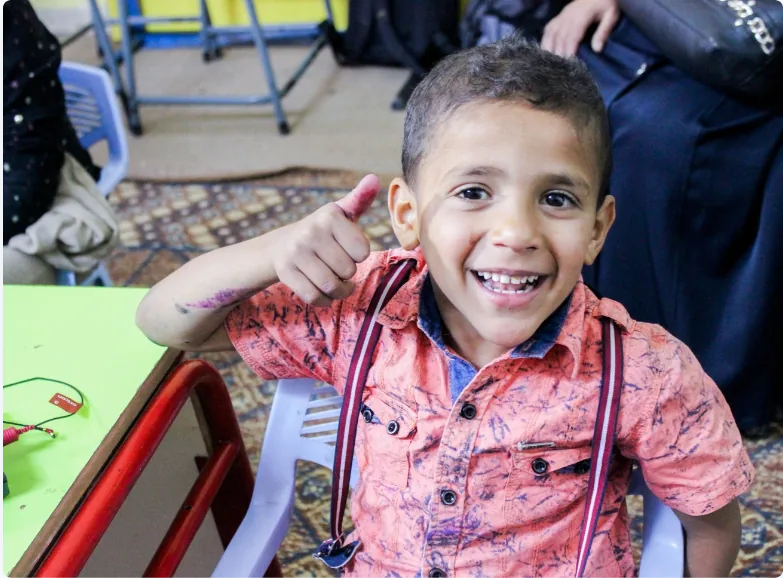 Young boy in orange shirt giving thumbs up at community space