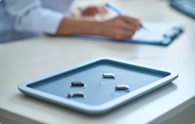 Hearing aids on blue tray with audiologist writing notes