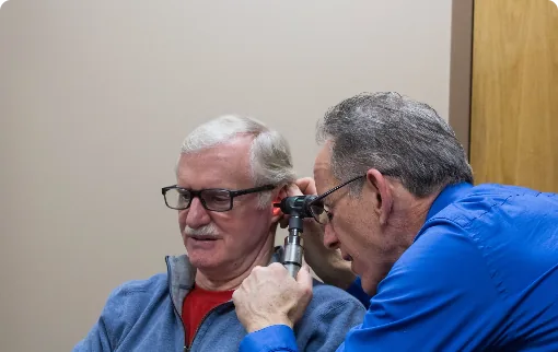Doctor examining elderly patient ear with otoscope