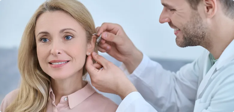 Audiologist fitting hearing aid on smiling woman