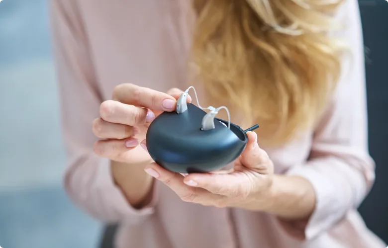 Woman holding behind-the-ear hearing aids on charging case