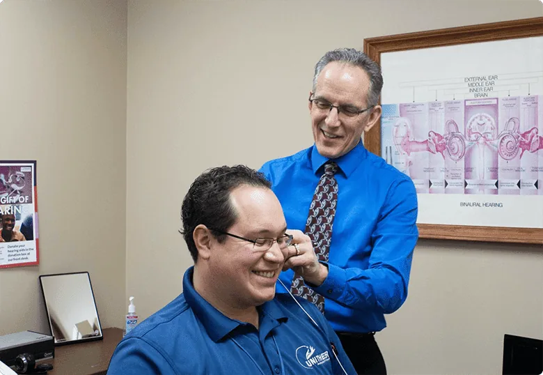 Audiologist fitting hearing aid on male patient with ear anatomy poster