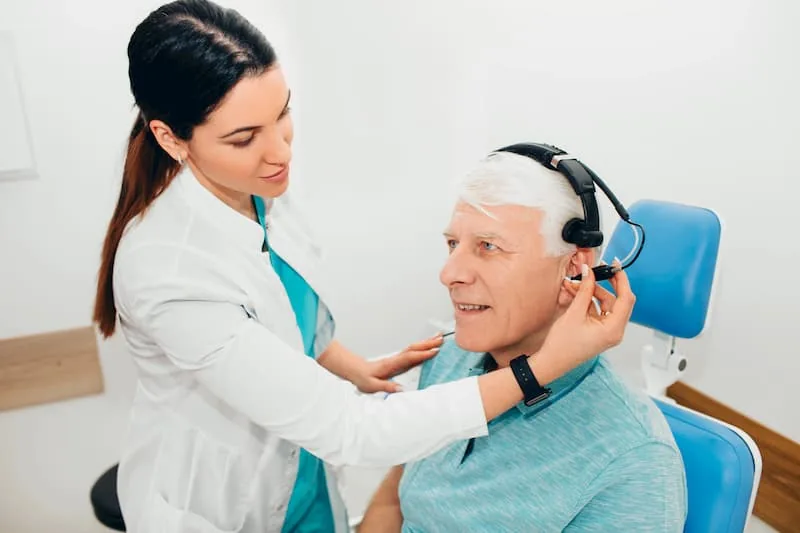 Audiologist fitting hearing device on senior male patient