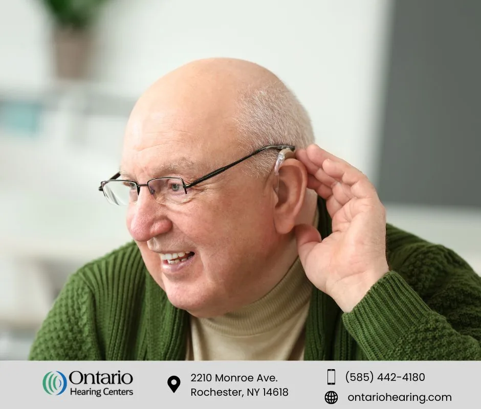 Older man with hearing aid cupping hand behind ear to listen