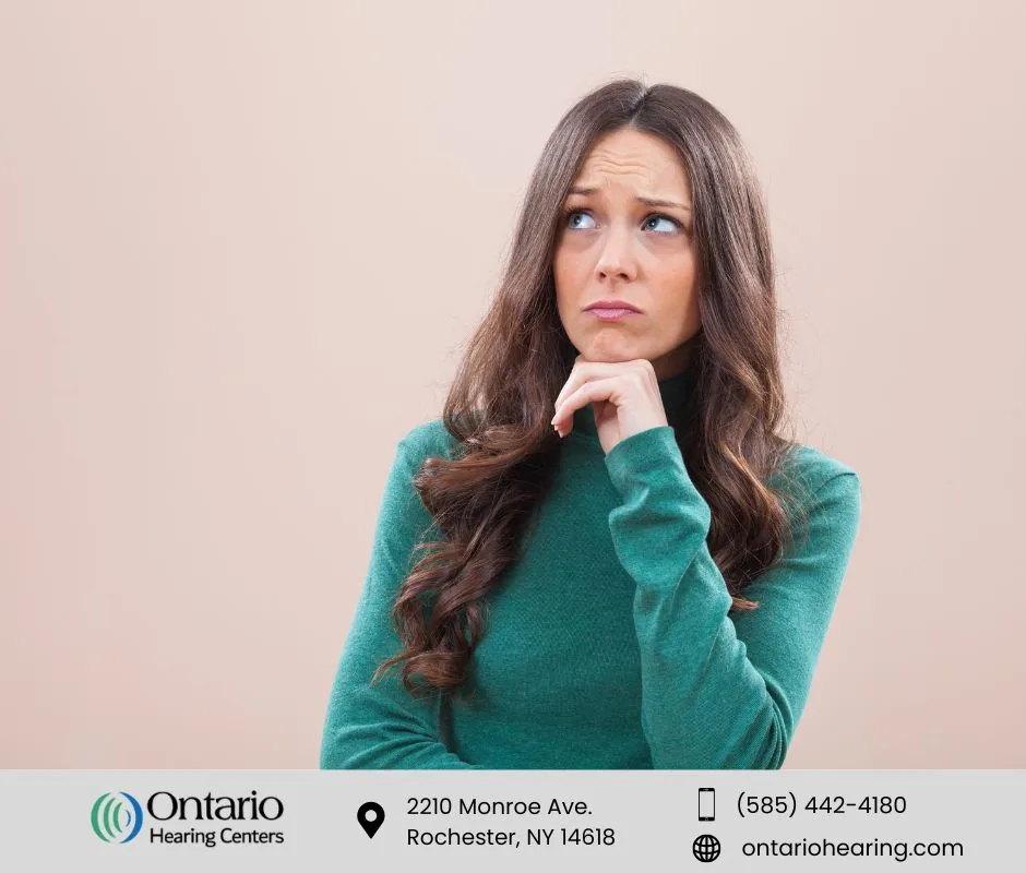 Woman in green turtleneck with concerned expression thinking about hearing aids