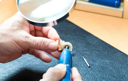 Technician cleaning hearing aid with rotary tool and magnifier