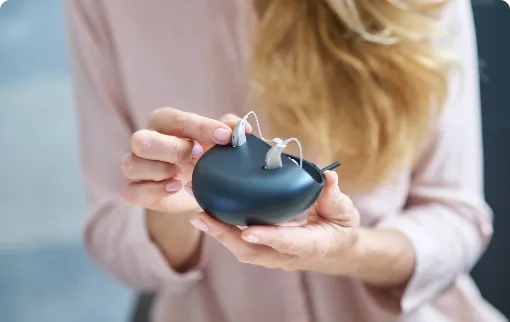 Woman holding hearing aids on decorative stand