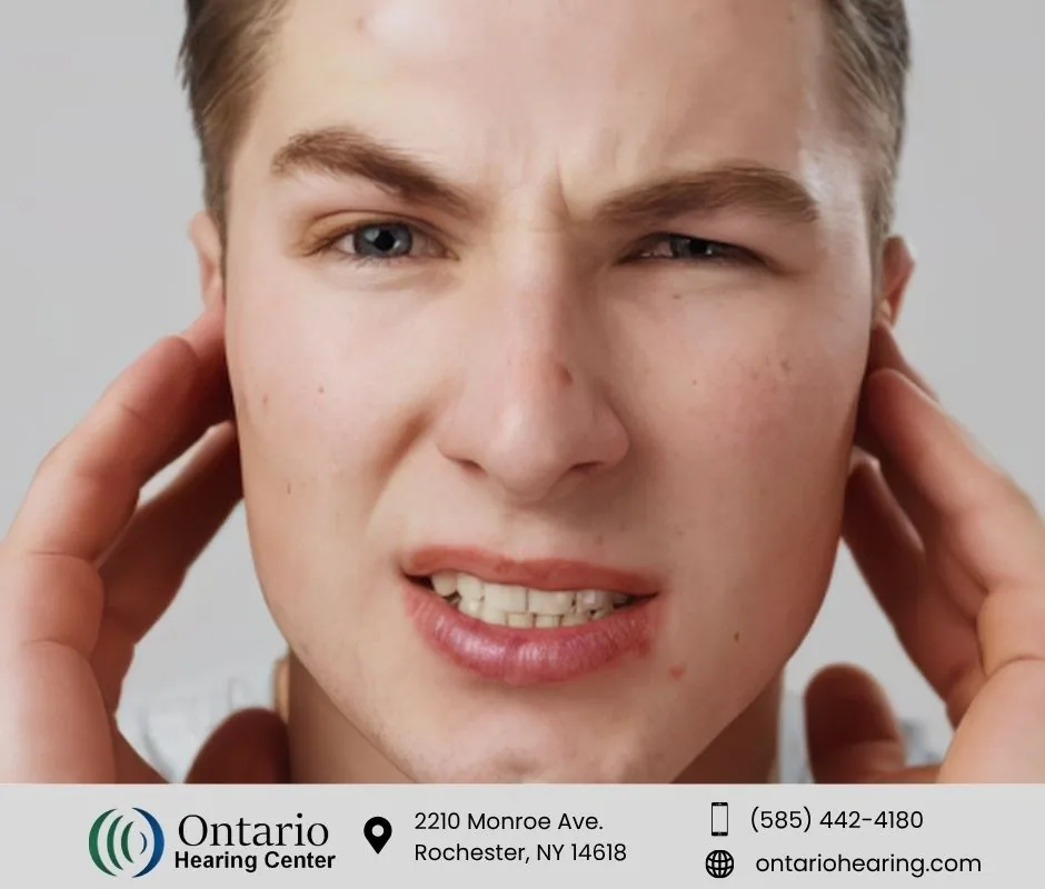 Man wincing while pressing both ears in discomfort