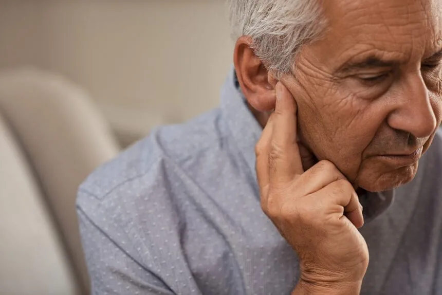 Older man touching ear with concerned expression about hearing