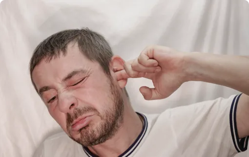 Man with goatee wincing while putting finger in ear