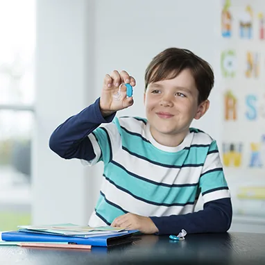 Young boy with hearing aid smiling in classroom