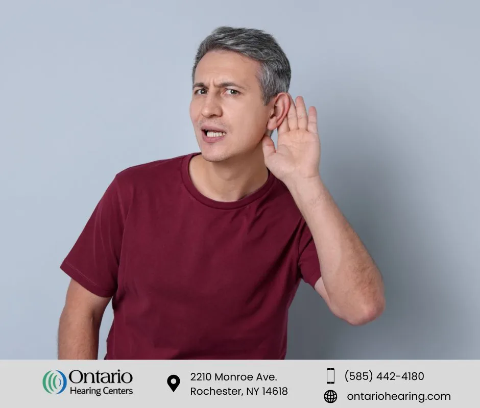 Man with grey hair wearing a red shirt, straining to hear with hand cupped to his ear.