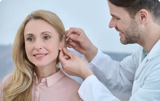 Male audiologist fitting hearing aid into woman ear