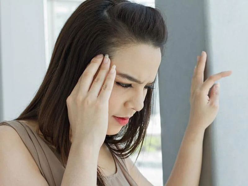 Woman holding temple bracing against wall experiencing vertigo