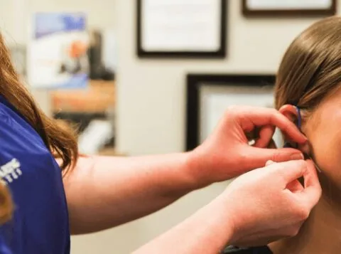 Healthcare professional fitting hearing aid into patient ear