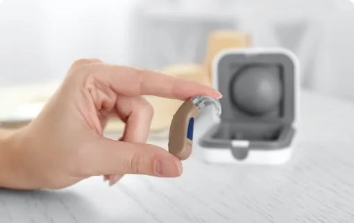 Hand holding beige behind-the-ear hearing aid with case