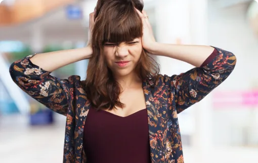 Woman covering ears with hands grimacing from loud noise